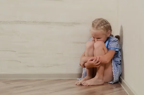 Sad young girl sitting in corner — Stock Photo, Image