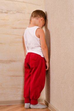 Little boy standing in a corner sulking clipart