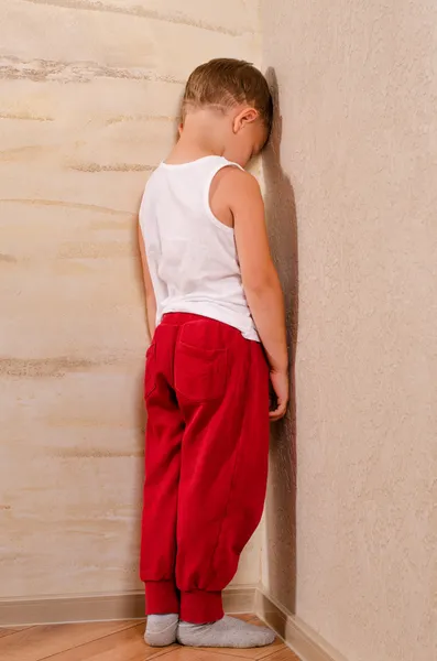 Petit garçon debout dans un coin boudant — Photo