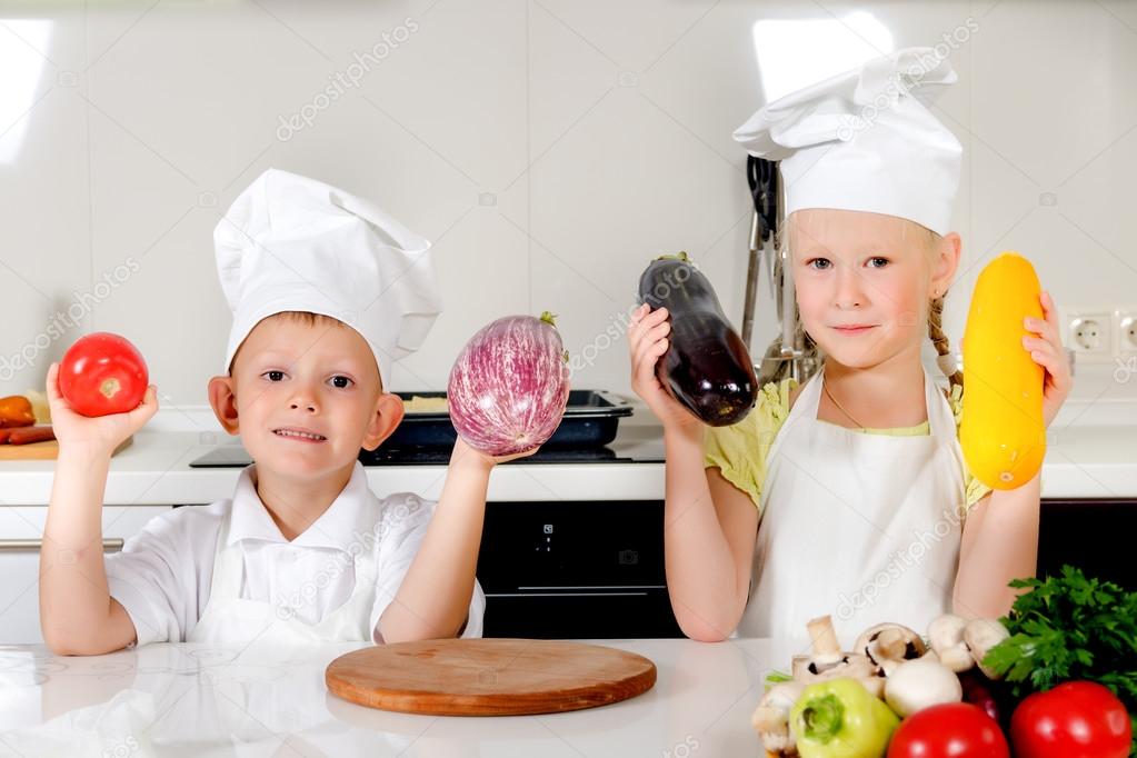 Two smiling children holding up fresh vegetables