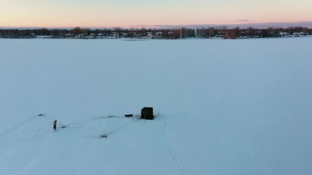 氷の上の漁師と白い雪に覆われた凍った川の小屋を示す空中ドローンは空中で撃たれました — ストック動画