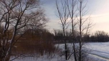 Çıplak ağaçlardan geçen bir İHA ile havadan yan uçuşlar ve kışın donmuş nehrin kıyılarını Laval-Ouest-24 fps 'teki Berges-des-quatre-vent' lerde gösteriyor.