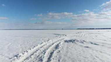 İnsansız hava aracı önce karın üzerinde alçaktan uçuyor. Yüksekten uçuyor. Uçurtma sörfçüsünü donmuş gölün daha ilerisinde gösteriyor.