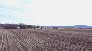 Düşük açılı insansız hava aracı, ilkbaharda boş bir tarla üzerinde geri uçmak, bazı dağları ve Mirabel yakınlarındaki Saint-Benoit 'teki bir yerleşim bölgesini gösteriyor.