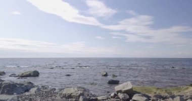 Aerial drone view flying mid-air over the sea, panning from right to left on a beautiful summer day over small waves