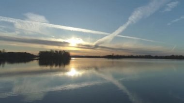 Aerial drone video of a dramatic golden sunset over calm waters with islands, a blue sky and some white clouds with lines done by aircrafts