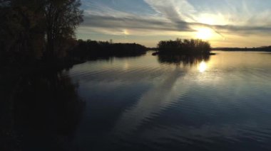 Aerial drone view, panning from left to right over the calm water of a river with a dramatic golden sunset