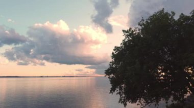 Aerial drone shot panning from right to left from behind a tree revealing the sunset with stormy clouds near the St-Lawrence river in Quebec