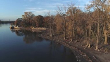 High angle drone video, over the calm water, near the shore, with people walking on the beach  and rotating from right to left