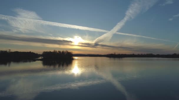 Almost still aerial drone video of a dramatic golden sunset over calm waters with islands, a blue sky and some white clouds with lines done by aircrafts
