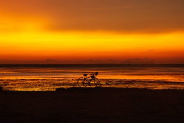 Kumsalda bisiklet ve miğferin silueti Sabah güzel turuncu gökyüzüne karşı.