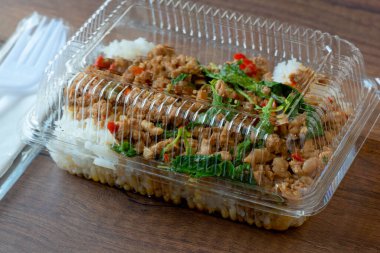 Tahta arka planda plastik bir kutuda domuz kıymalı fesleğenli pilav..