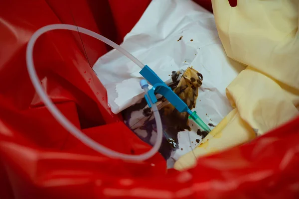 Needle with plastic tube and used surgical glove in garbage bin in operating room