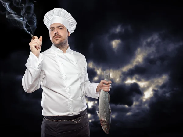 Junger Koch mit Wolfsbarsch, der Zigarre raucht — Stockfoto