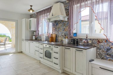 Beyaz dolapları ve renkli fayansları olan geniş bir mutfak. Klasik modern tarz.