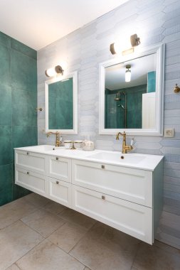 Yeşil ve açık mavi fayanslı iki lavabosu olan küçük bir banyo.