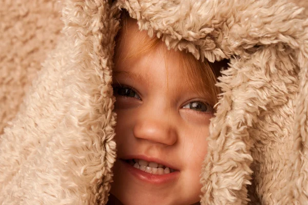 Smiling toddler hiding in fur blanket — Stock Photo, Image