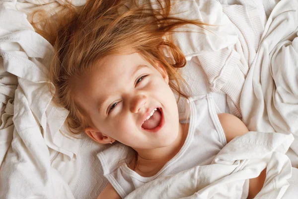 Happy little girl laying in white laundry — Stock Photo, Image