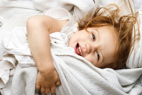 Happy young child rolling in white covers — Stock Photo, Image