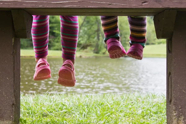 Pequeños pies colgando de un banco en un estanque —  Fotos de Stock