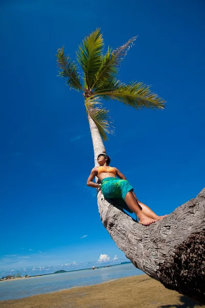 Jonge vrouw leunend tegen kokosnoot boom door een tropisch strand — Stockfoto