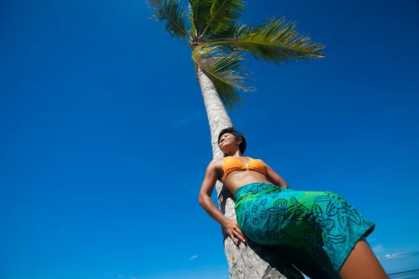 Mooie jonge vrouw leunend tegen kokosnoot boom op tropisch strand — Stockfoto