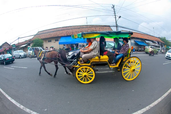 JOGJAKARTA 15 MAIO. Carruagens puxadas a cavalo são método popular de transporte nas ruas movimentadas de Jogja. Uma família em uma carruagem puxada a cavalo nas ruas Fotos De Bancos De Imagens