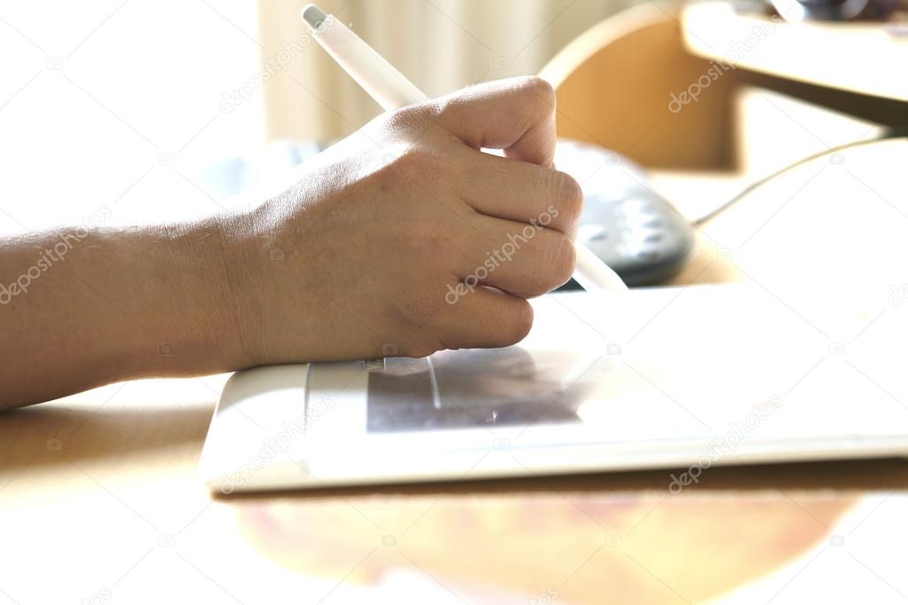 Hand holding stylus pen while working on tablet attached to computer.