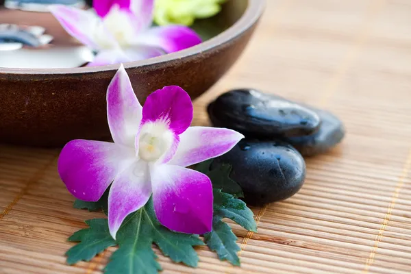 Piedras de spa con orquídeas y tazón de agua —  Fotos de Stock