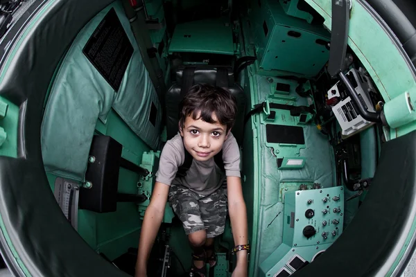 Glada unga pojken som sitter i en tank på armén öppet hus. — Stockfoto