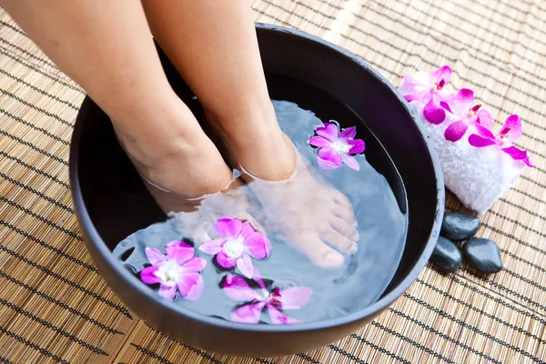 Vrouw voeten in voet spa kom met orchideeën — Stockfoto