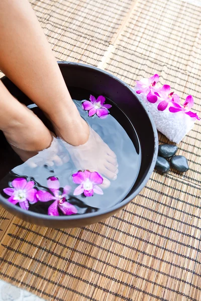 Pés de mulher em tigela spa pé com orquídeas — Fotografia de Stock