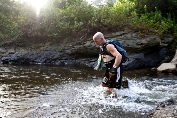 Un coureur d'une équipe participante fait son chemin le long d'une rivière — Photo