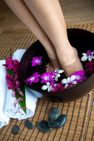 Vrouwelijke voeten in voet spa kom met orchideeën Stockafbeelding