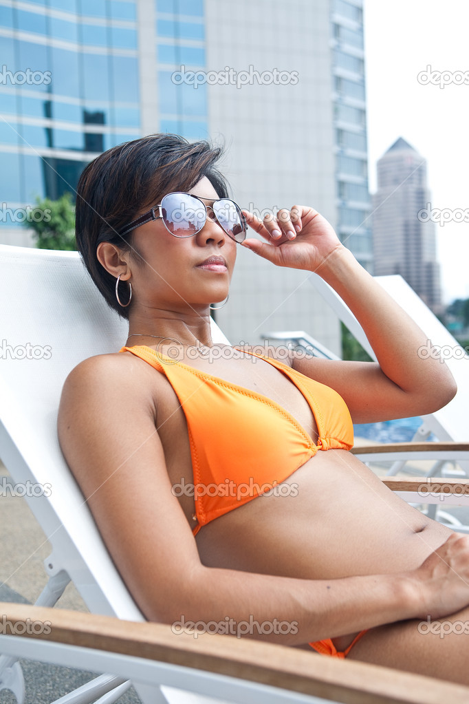 Beautiful Asian woman in orange bikini relaxing by the pool