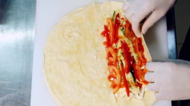 Cook, Pita 'yı dolgu malzemesiyle paketliyor. Eldivenli bir şefin elleri taze sebzeli lezzetli pide pişiriyor. Fast food restoranında lezzetli atıştırmalıklar yapma süreci. Yakın plan..