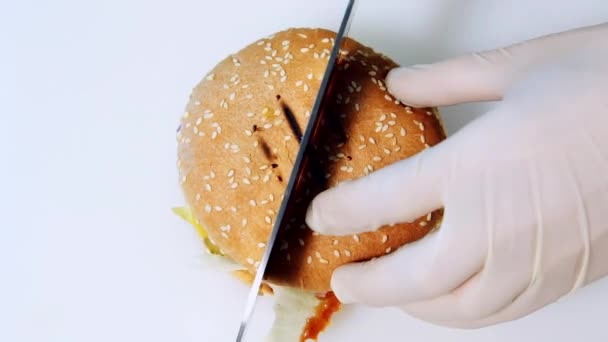 把现成的汉堡包切成两半 厨师用锋利的金属刀积极地在白色背景上切一个新鲜的汉堡 顶部视图 — 图库视频影像
