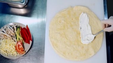 Fast food restoranında yemek pişirme süreci. Şefin elleri kaşıkla mayonez yayıyor ve Pita 'nın üstüne tavuk eti koyuyor. Üst görünüm.