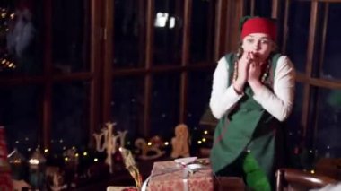 Heyecanlı elfler ve Noel hediyeleri. Masaya hediye kutuları koyan komik kadın ve erkek elfler. Noel dekore edilmiş oda arka planı.