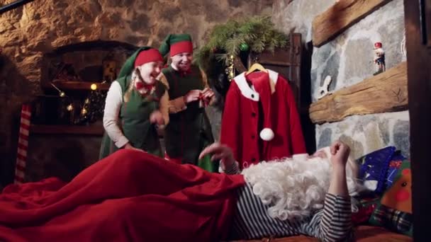眠いサンタとエルフ 陽気エルフはクリスマスに特別な装飾された部屋で彼の寝室でサンタを目覚めさせます サンタはクリスマスの夜彼のベッドから取得 — ストック動画