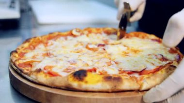 Pizza turtası dilimleniyor. Aşçı, ahşap masada pizza dilimlemek için yuvarlak kesici bıçak kullanıyor..