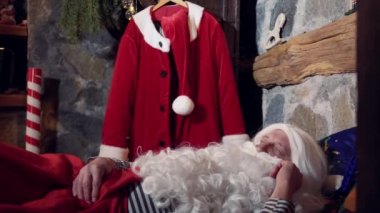 Santa with white beard sleeping in his residence. Funny elves ringing with a little bell to wake up Santa. Christmas time.