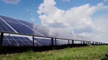 Walk along a row of photovoltaic solar panels. Solar power plant in the field. Bottom view of the sky with clouds.
