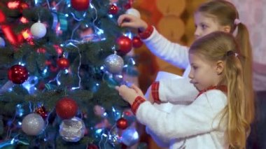 Two cute little girl sisters decorate the Christmas tree with red and white balls. Holidays and celebrations concept.