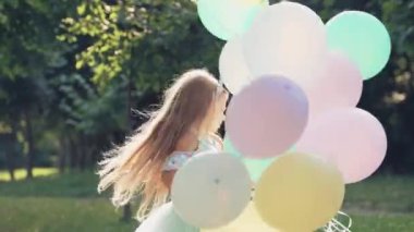 Küçük kız parkta elinde balonlarla dönen oyunlar oynuyor. Renkli balonları olan bir çocuk..