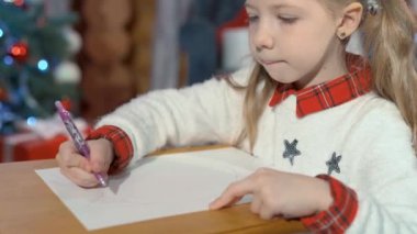 Şirin küçük kız evde kağıt üzerine kalemle kedi resmi çiziyor. Noel ağacının arka planında bir odada bir çocuğun portresi.