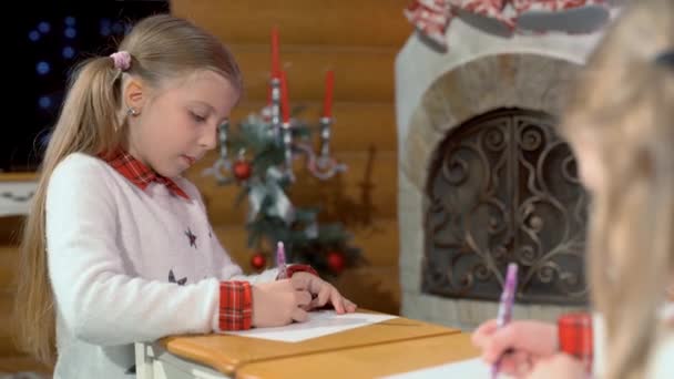 소녀들은 난로와 크리스마스 근처에 테이블에서 그림을 그립니다 새해가 산타클로스에게 편지를 — 비디오