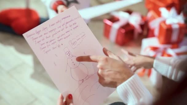 女性の手に雪男と子供の願いの写真と紙の作品 サンタクロースへの手紙 背景にある箱の中のクリスマスプレゼント — ストック動画