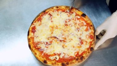 Masada İtalyan pizzasını dilimlemek. Yuvarlak pizza kesicisi. Yukarıdan bak. Beyaz eldivenli aşçının elleri..