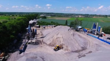 Çalışan asfalt bitkisi. Kazıcı asfalt üretimi için ezilmiş taş topluyor. Bacadan duman çıkıyor. Bir yol kaldırım fabrikasının havadan görünüşü.